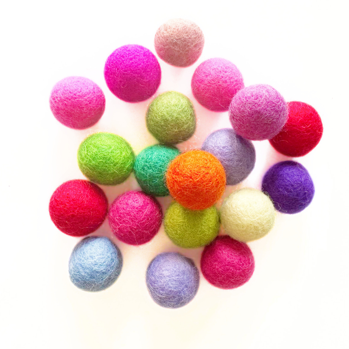 A cluster of colourful felt balls in various shades including pink, green, orange, purple, blue, and red, arranged on a plain white background.