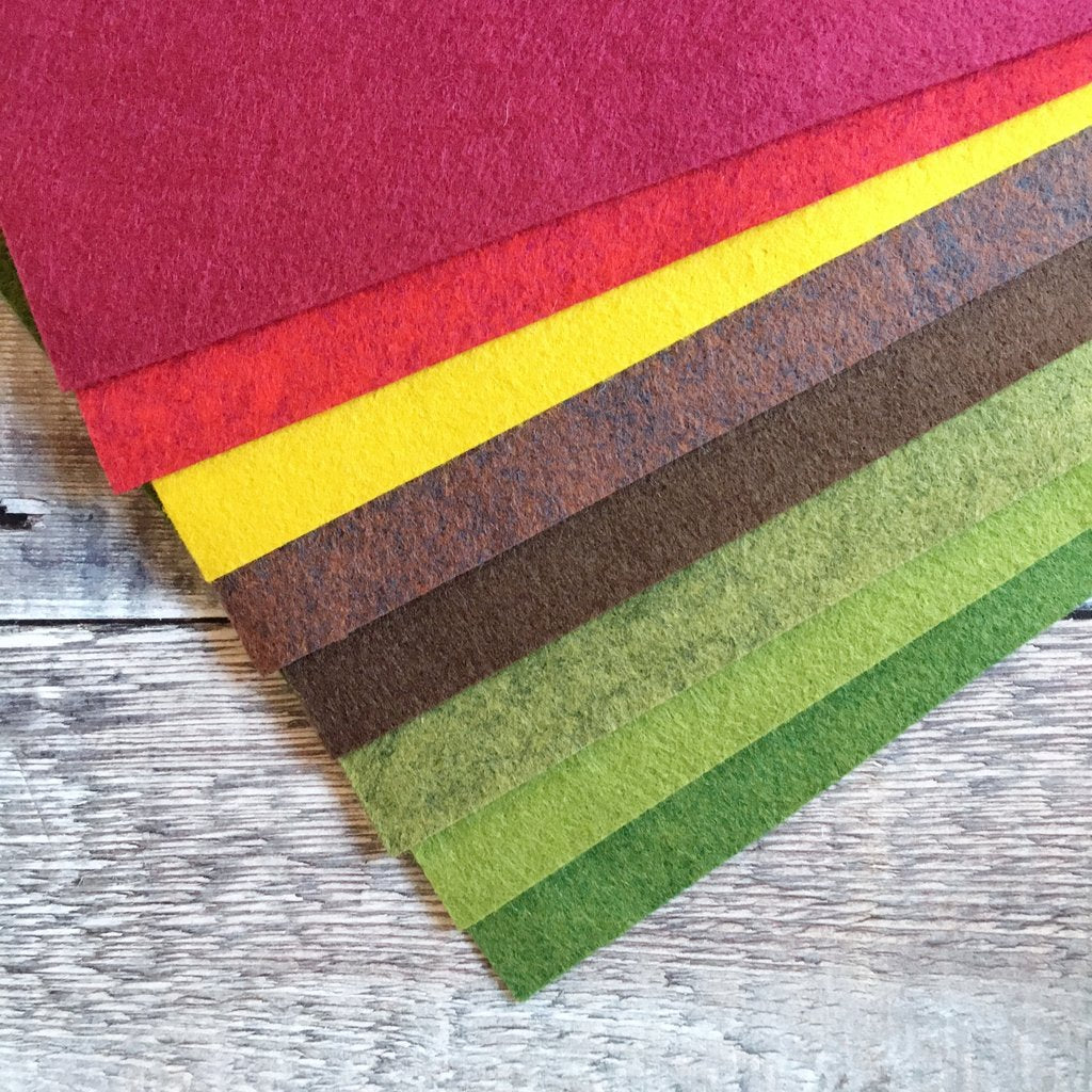 A selection of felt sheets in various colours including garnet, red, gold, brown, and green, arranged on a wooden surface.
