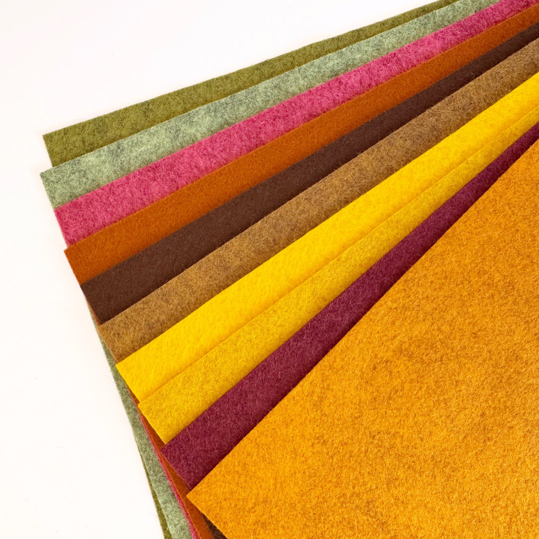A fan arrangement of textured felt sheets in multiple colours, including green, pink, orange-brown, dark brown, gold, and mustard yellow, on a white background.