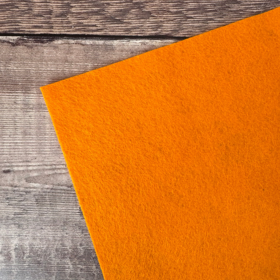 Bright orange felt laid diagonally on a rustic gray wood plank surface.