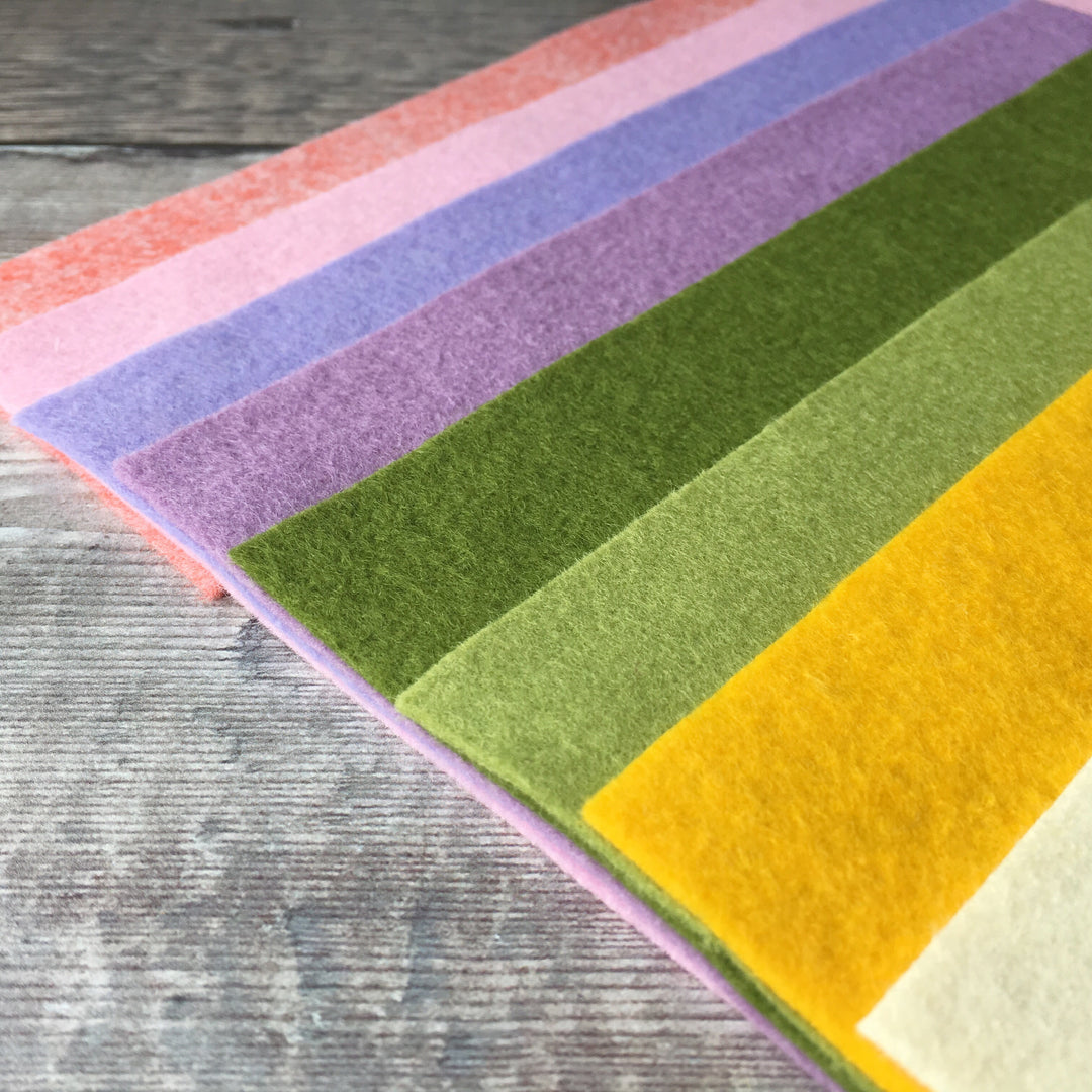 A selection of colorful wool-blend felt sheets arranged in stripes of different colors, including gold, green, yellow, pink, purple, and lilac.