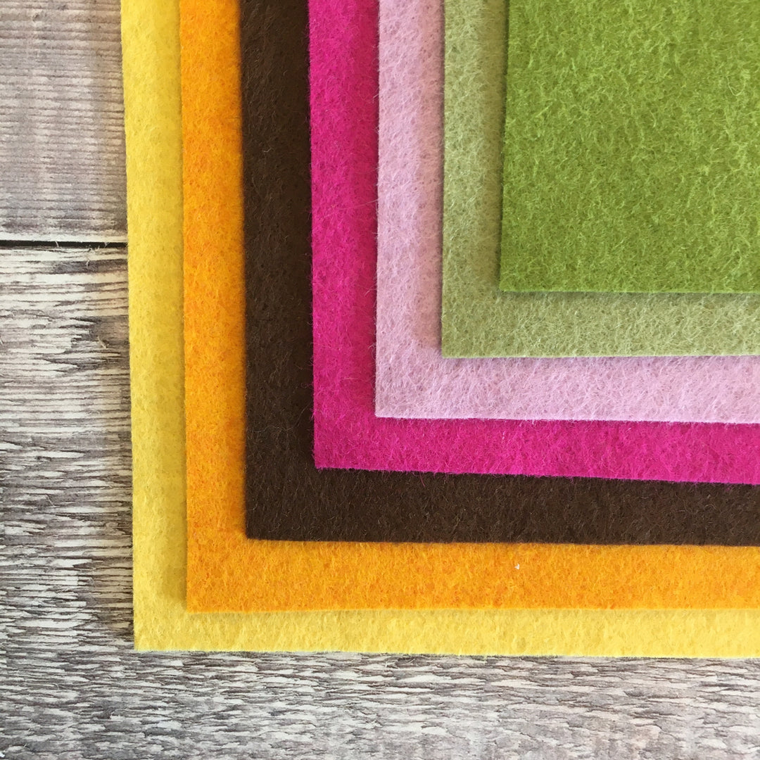 A collection of felt sheets in various colors including yellow, orange, brown, pink, purple, green, and blue, laid out on a wooden surface.
