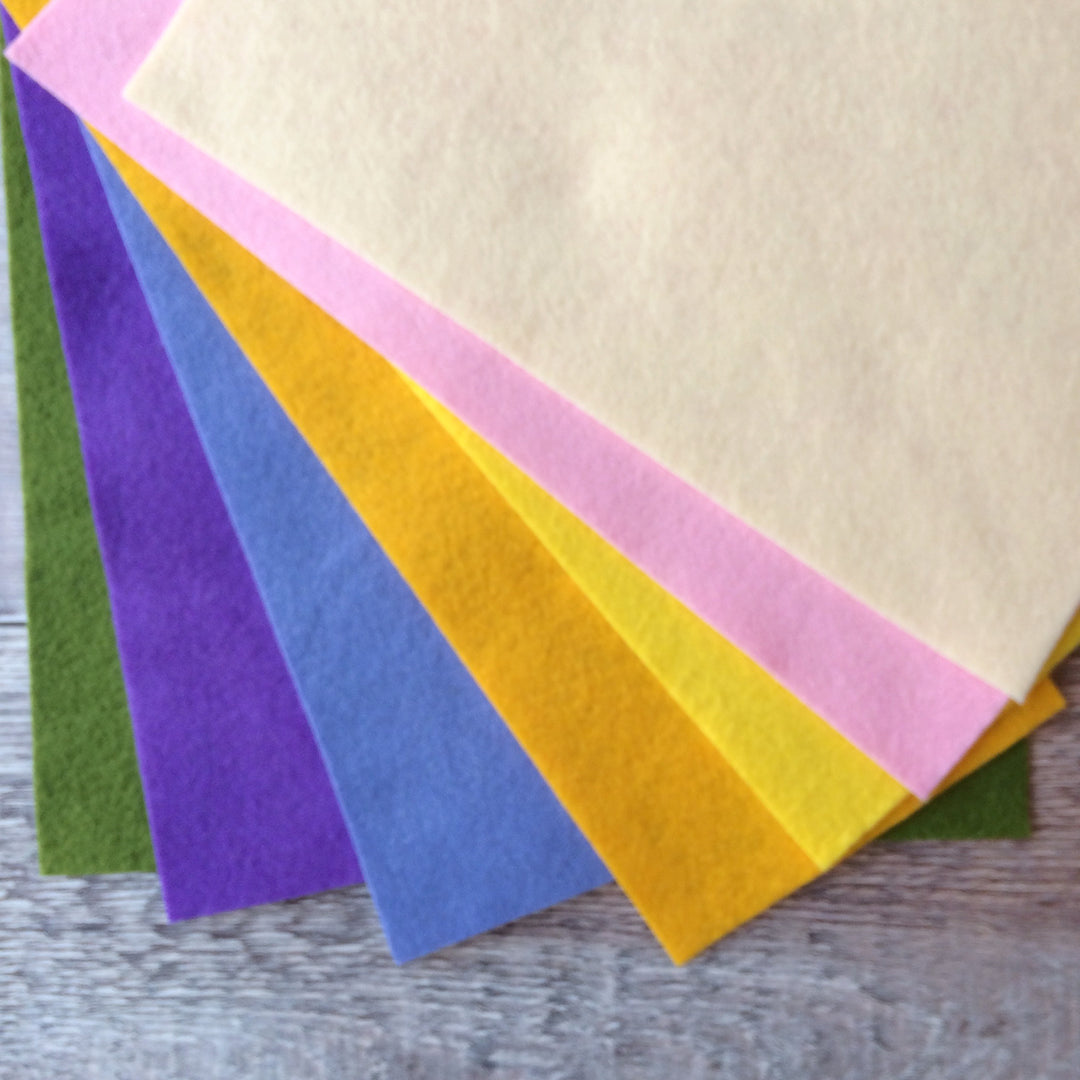 A stack of various colored felt sheets including straw, pink, yellow, gold, blue, lavender, and green.